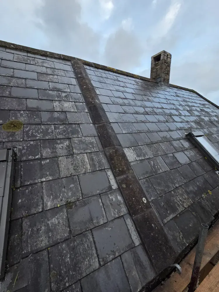 Weathered slate roof with a stone chimney, viewed up the slope